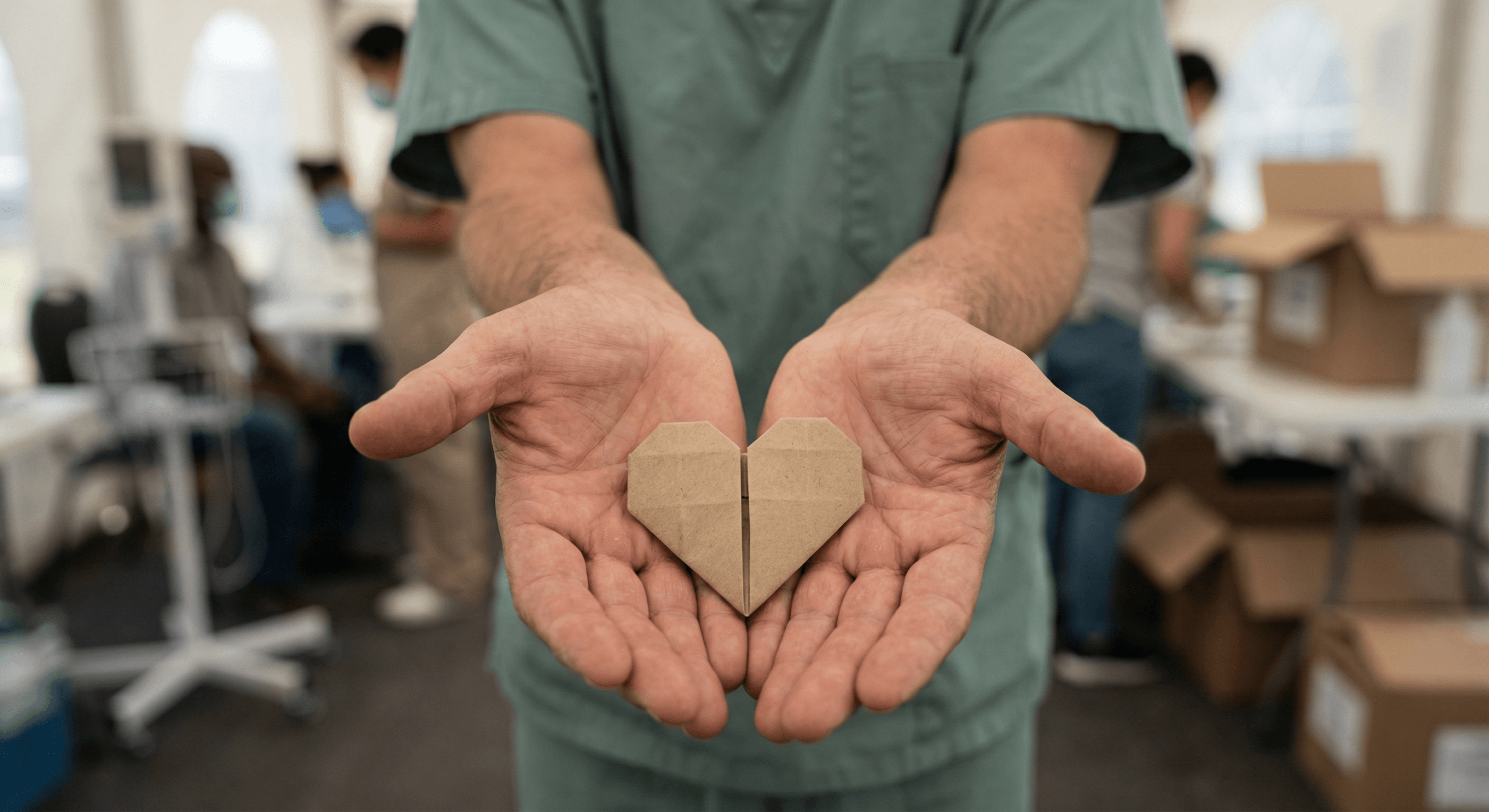 A healthcare worker’s open hands hold a delicate paper heart, symbolizing care, vulnerability, and hope within fragile humanitarian settings.