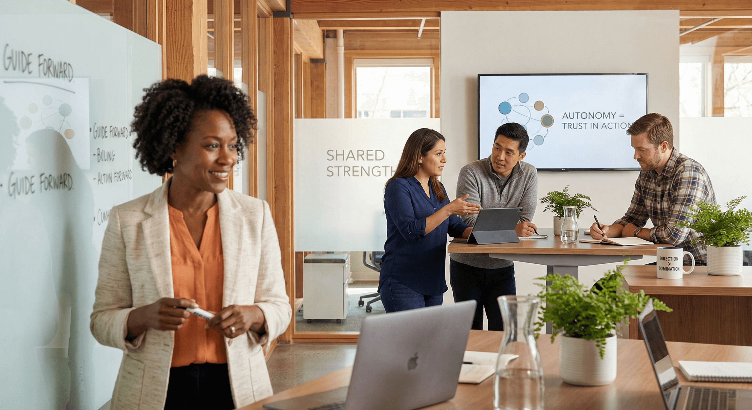A team leader stands smiling beside a whiteboard while her coworkers collaborate independently in bright natural light, embodying delegating without guilt and the confidence to lead by trust rather than control.