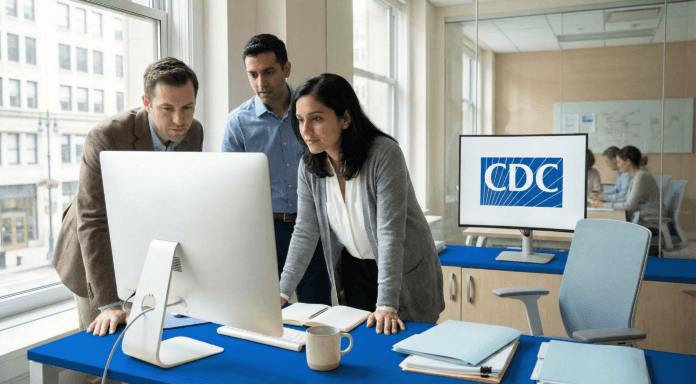 Three public‑health researchers review data charts on a computer screen in a bright modern office with a CDC logo visible in the background.