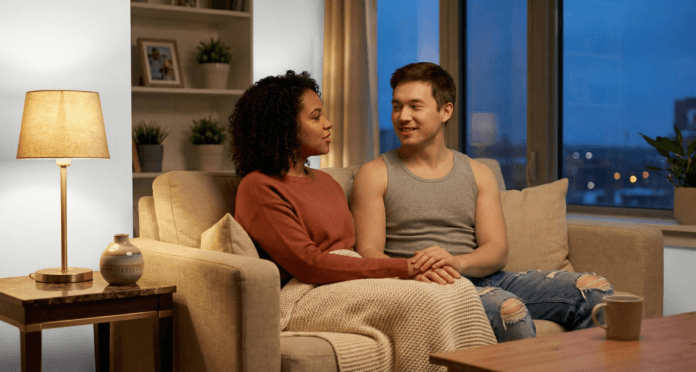 A married couple sits close together on a softly lit couch, hands gently joined as they talk with empathy and warmth, portraying intimacy in marriage through calm communication, trust, and emotional presence.