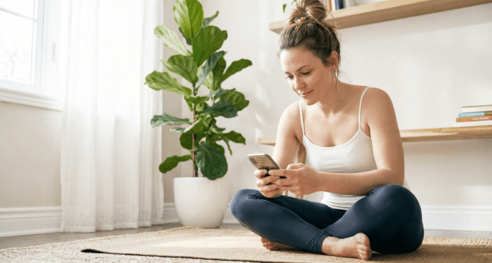 woman-selecting-meditation-app-session-yoga-mat.jpg Man sitting on couch with slight smile looking at smartphone screen browsing dating profiles in evening light